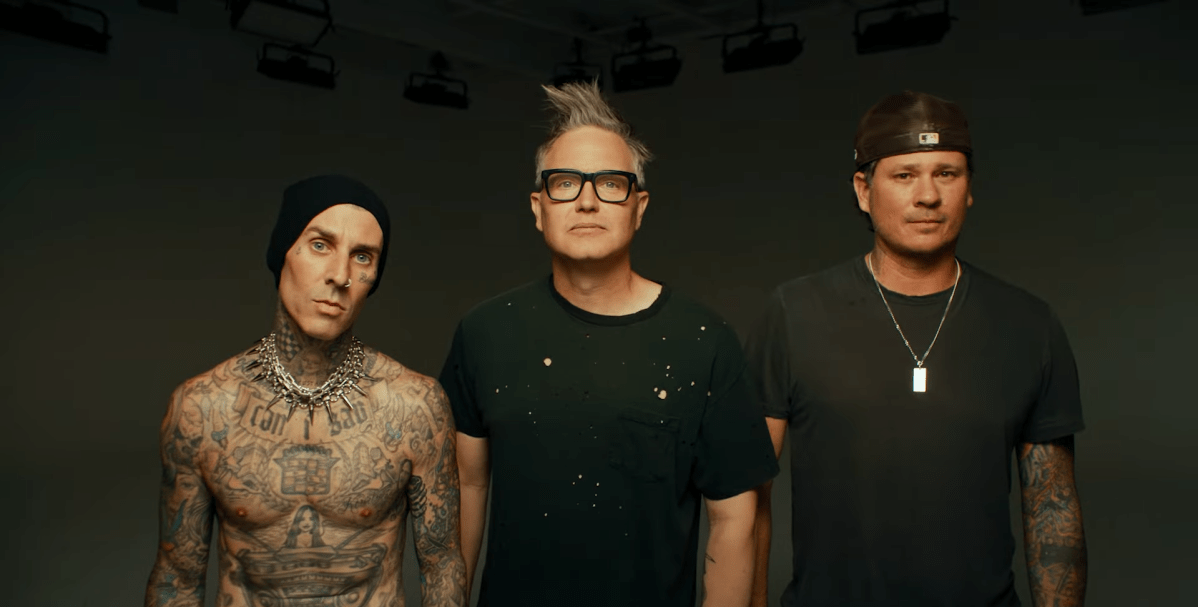 Tom DeLonge, Mark Hoppus and Travis Barker pose. Barker is shirtless. DeLounge and Hoppus wear black tees.
