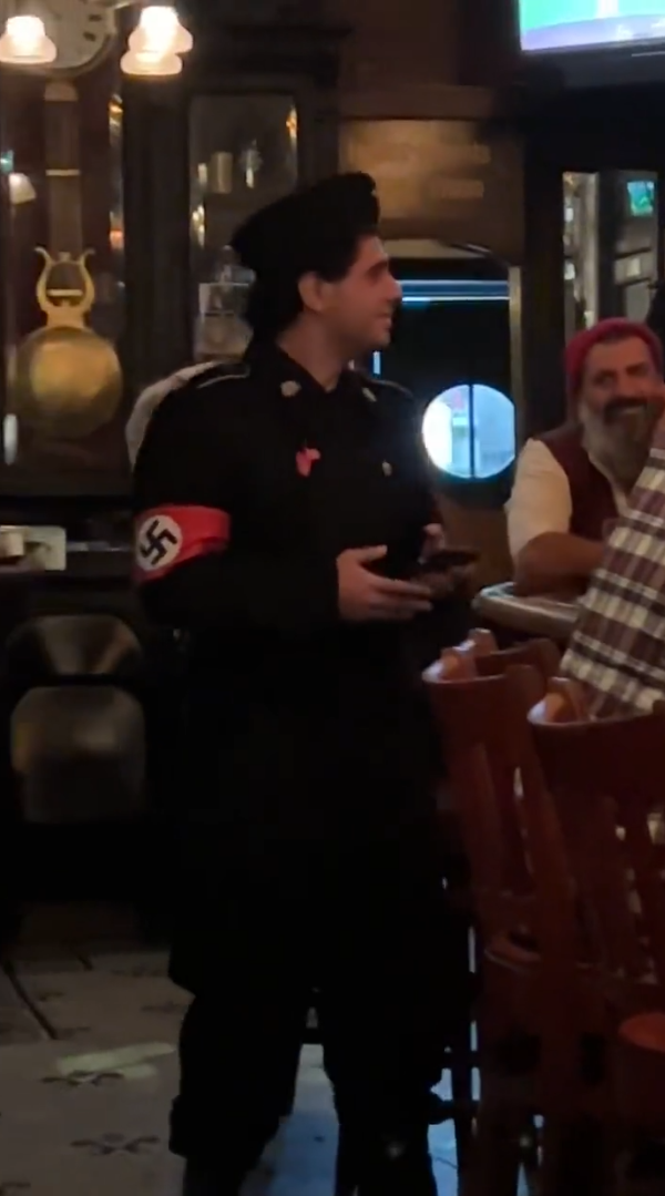 A man dressed in a Nazi costume stands in a dimly lit bar.