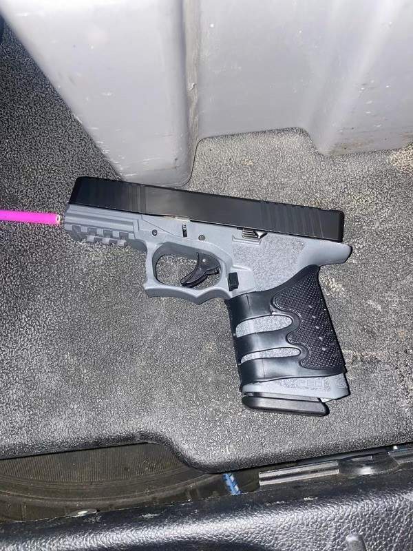 A handgun laid on the floor. Beside the barrel is the tip of a pink coloured pencil.