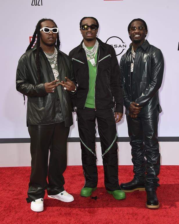 All three Migos members stand on a red carpet.