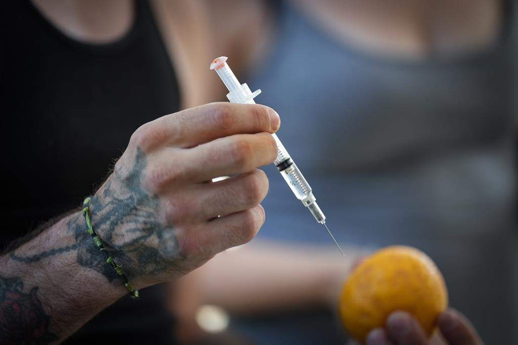 A person holds a syringe and an orange while learning how to administer Naloxone to an overdose victim, during an International Overdose Awareness Day gathering in Surrey, B.C., on Wednesday, Aug. 31, 2022.