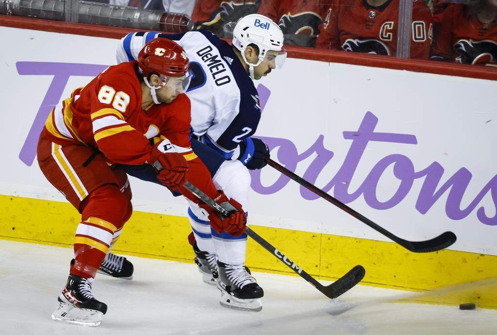 Winnipeg Jets defenceman Dylan DeMelo, right, and Calgary Flames forward Andrew Mangiapane chase the puck during second period NHL hockey action in Calgary, Alta., Saturday, Nov. 12, 2022.