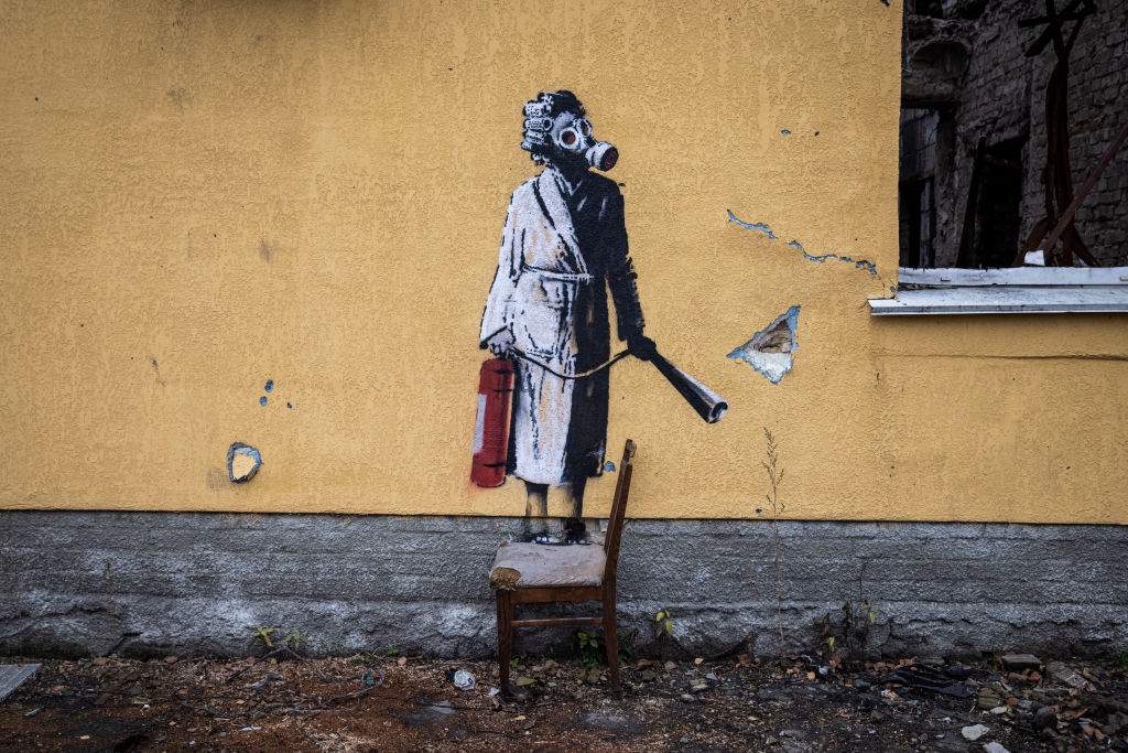 Street art of a person in a dressing gown holding a fire extinguisher and wearing a gas mask is painted on a wall of a destroyed building in Hostomel near Antonov Airport on November 12, 2022 in Kyiv Region, Ukraine.