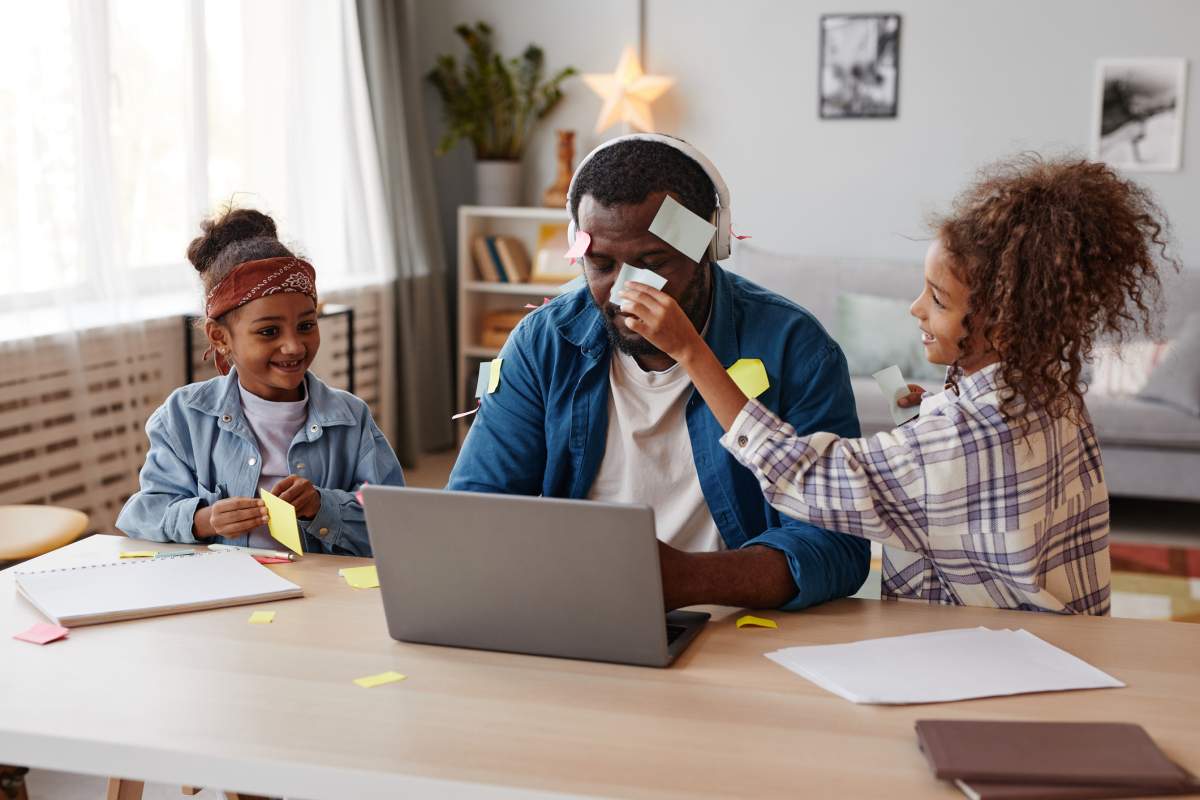 Photo of two girls annoying their dad while he's trying to work