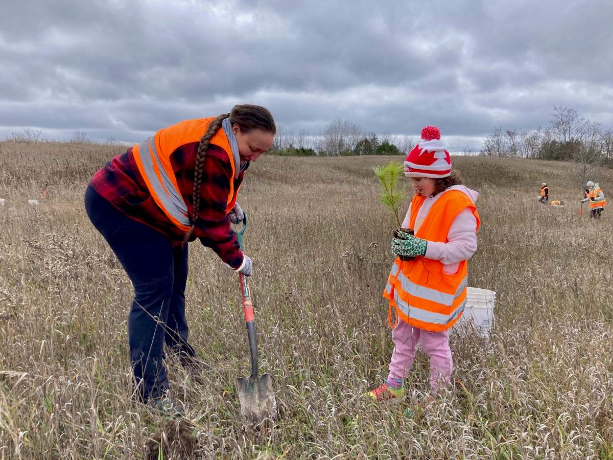 Janique Labelle (left) helps Aryanne Labelle dig a hole to plant a tree at a former gravel pit site in Ennismore, Ont.