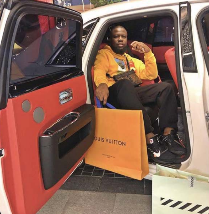 Ramon Abbas sitting in a car, holding a Louis Vuitton shopping bag.