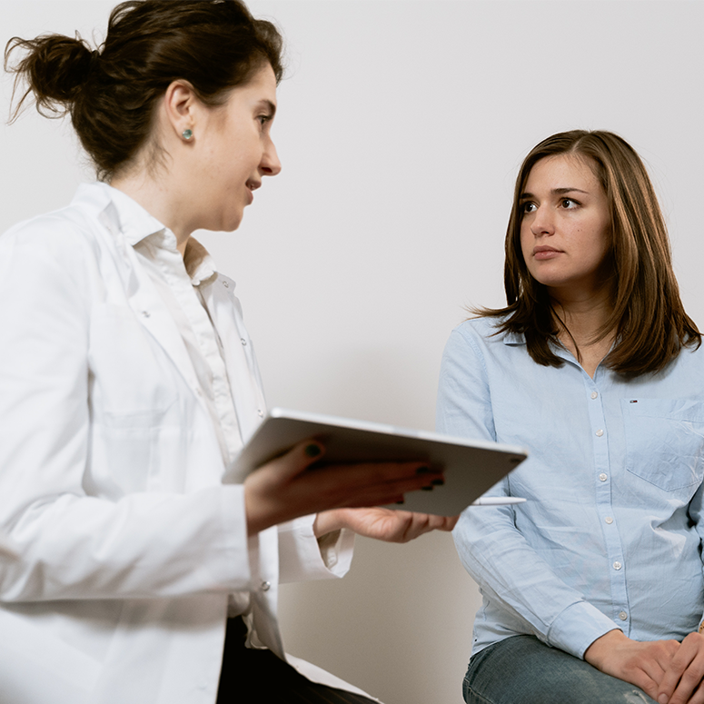 A doctor holds a tablet screen while talking to a patient