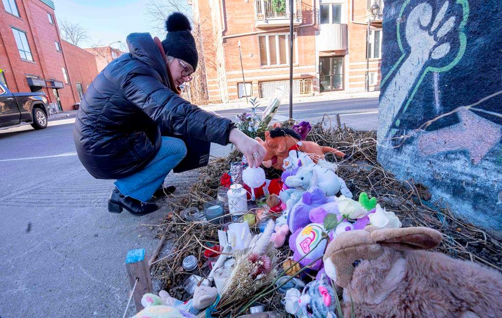 A woman places a candle at a makeshift memorial on Wednesday, Dec. 14, 2022, on the corner where a seven-year-old girl was killed in a hit and run in Montreal.