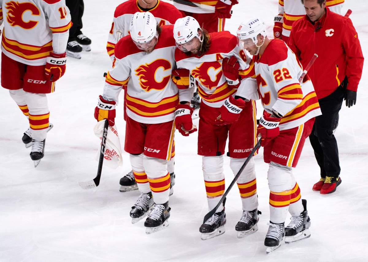 Calgary Flames’ Chris Tanev is helped off the ice by teammates Rasmus Andersson, left, and Trevor Lewis after taking a puck to the head during second period NHL hockey action against the Montreal Canadiens in Montreal, Monday, Dec. 12, 2022.