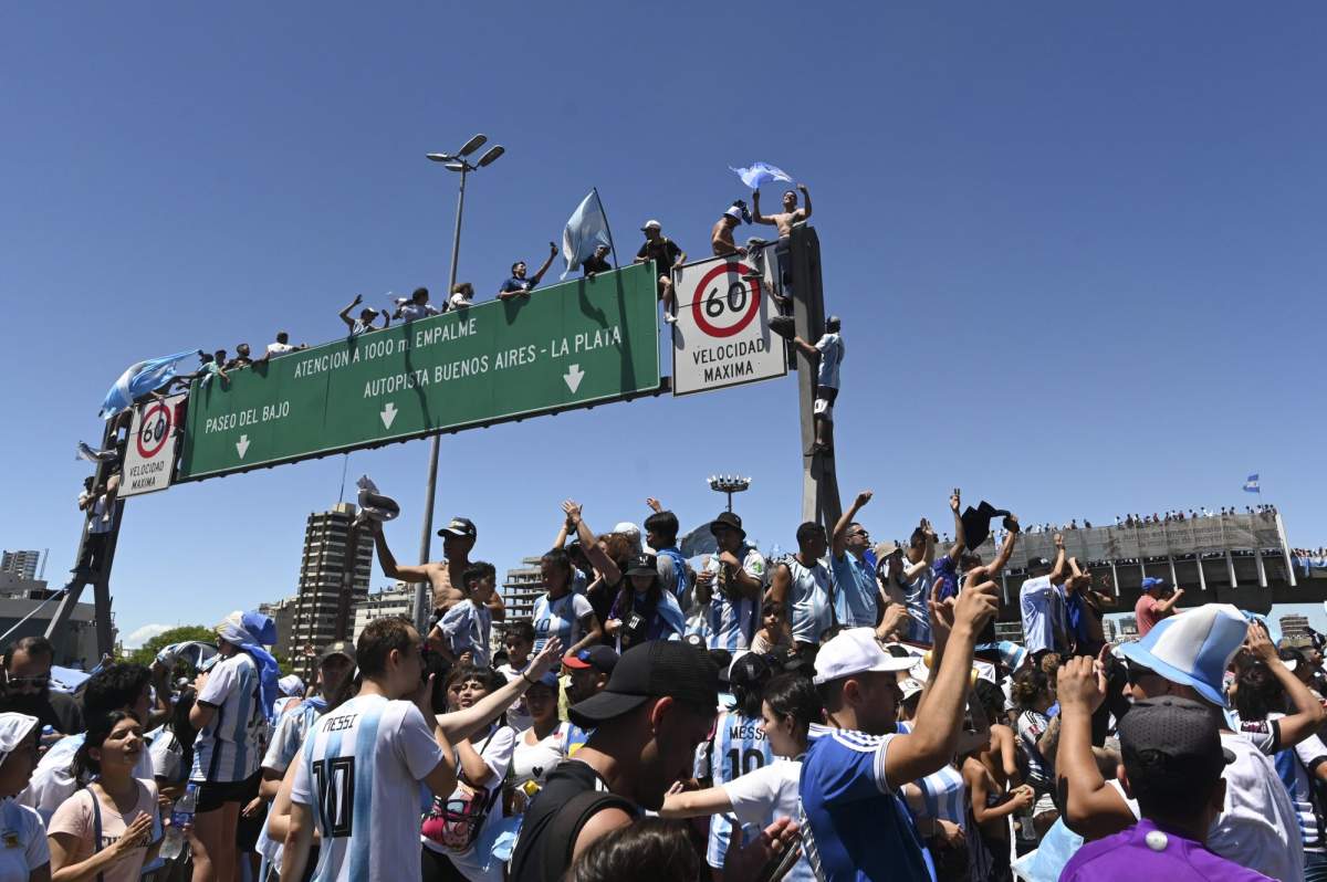 Argentine soccer fans climb on highway signs for a homecoming parade for the Argentine soccer team that won the World Cup tournament in Buenos Aires, Argentina, Tuesday, Dec. 20, 2022.