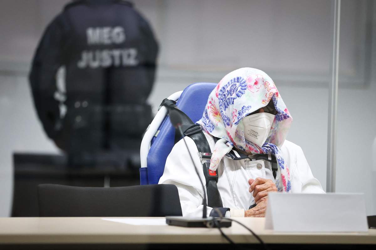 Irmgard Furchner wearing a mask, sunglasses and a scarf on her head. She is buckled in to her wheelchair.