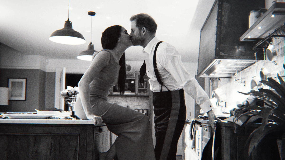 A still shot from "Harry & Meghan." The couple is seen kissing in a kitchen.