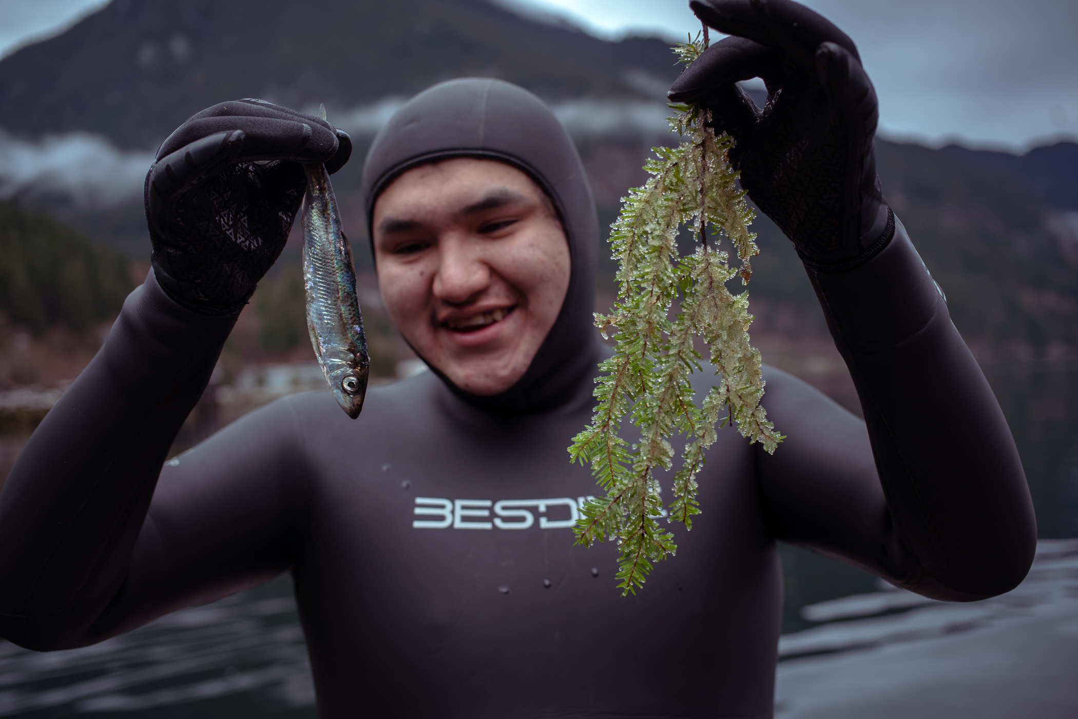 Jonathan Williams, an Indigenous youth snorkeler with the Squamish Nation holds up a herring and a cedar bough. Williams was part of a team of 'citizen scientists' who are mapping the return of herring in Átl’ḵa7tsem-Howe Sound, B.C.