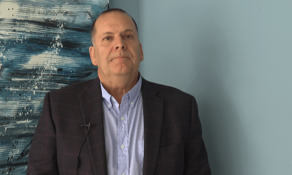 Chris Collins stands in front of a blue abstract painting.