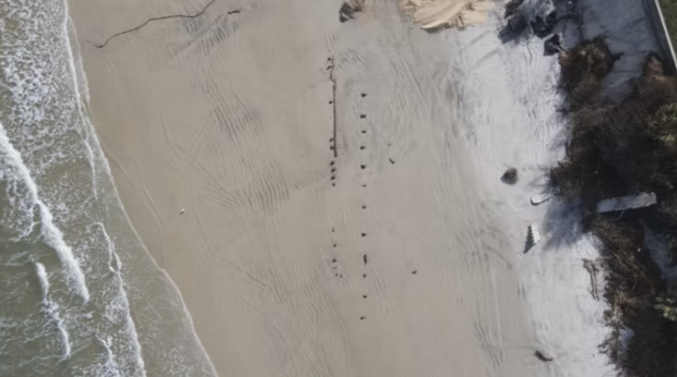 Objects protrude from the sand in this image taken from above.