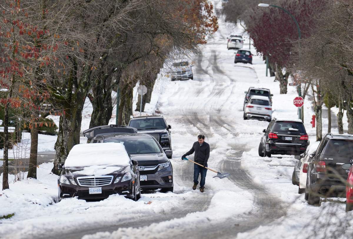 A man pauses while digging out snow from under a car stuck on a street in the aftermath of a snowstorm, in Vancouver, B.C., Wednesday, Nov. 30, 2022.