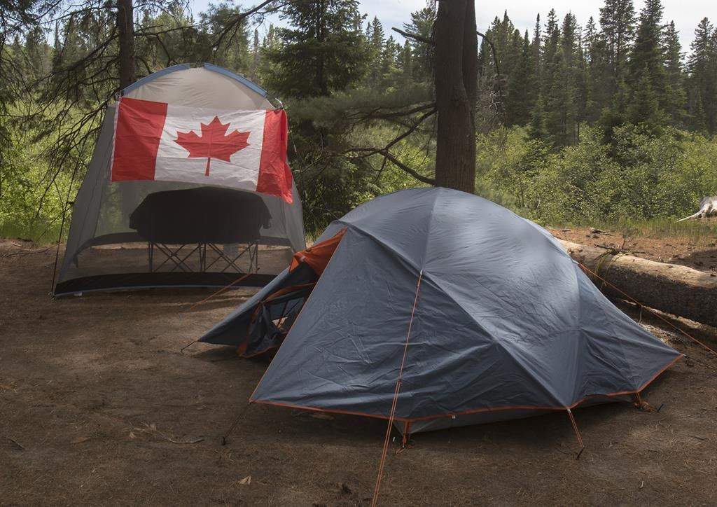 Campers with a Canadian flag flying on their camp site are shown in Algonquin Park on Saturday, June 12, 2021. Parks Canada says visitors will be able to start booking reservations for camping and other activities at its sites across the country in March. THE CANADIAN PRESS/Fred Thornhill.