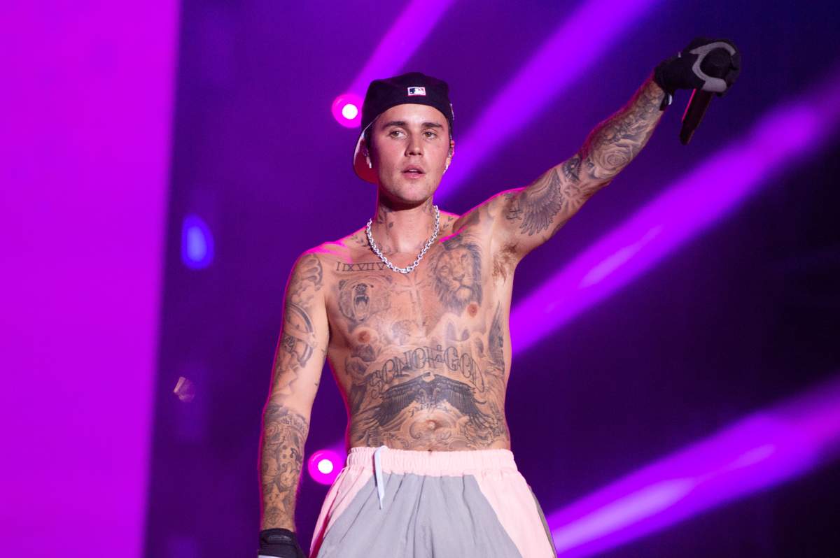 Justin Bieber on stage. He is shirtless and holding a microphone.