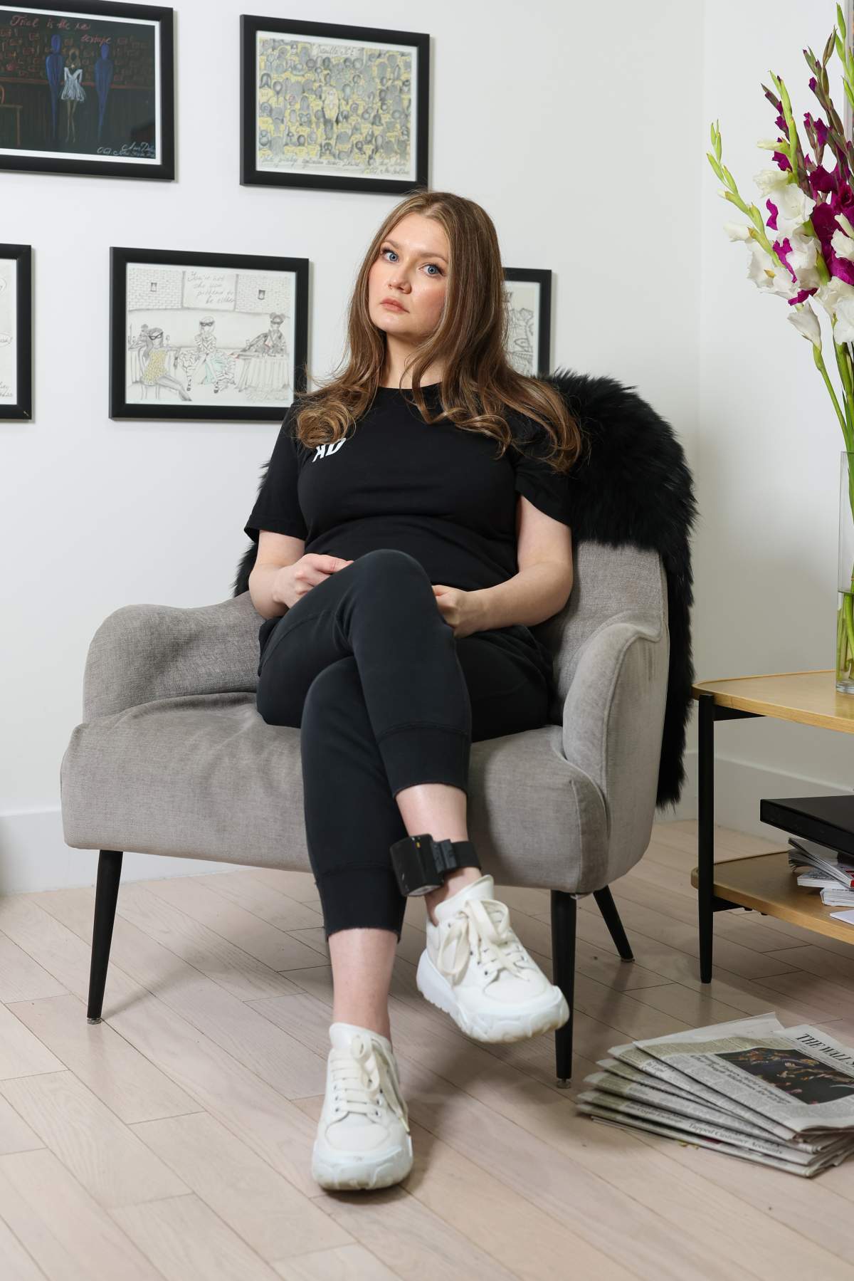 Anna "Delvey" Sorokin. She is wearing a black shirt, black pants and an ankle monitor.