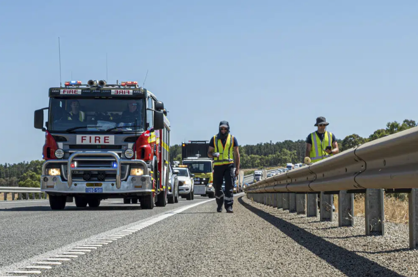 A firetruck and two people in high visibility vests walk alongside a road.