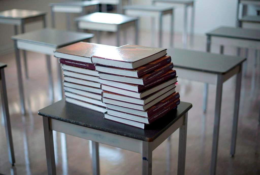 Books are piled onto a desk in an empty classroom at a high school
