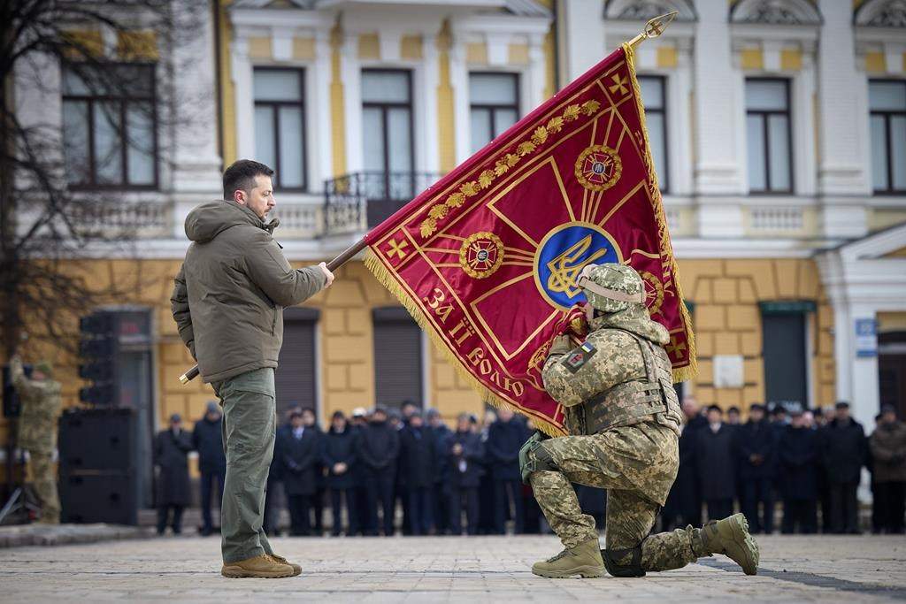 Ukrainian President Volodymyr Zelenskyy, left, holds the flag of a military unit as an officer kisses it, during commemorative event on the occasion of the Russia Ukraine war one year anniversary in Kyiv, Ukraine, Friday, Feb. 24, 2023.