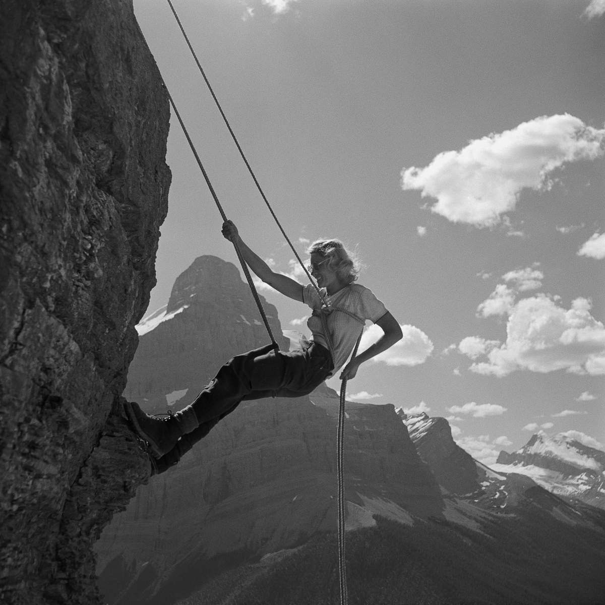 An unnamed woman rappels during the 1950 Alpine Club of Canada ACC camp at Maligne in a photograph by Harry Rowed.