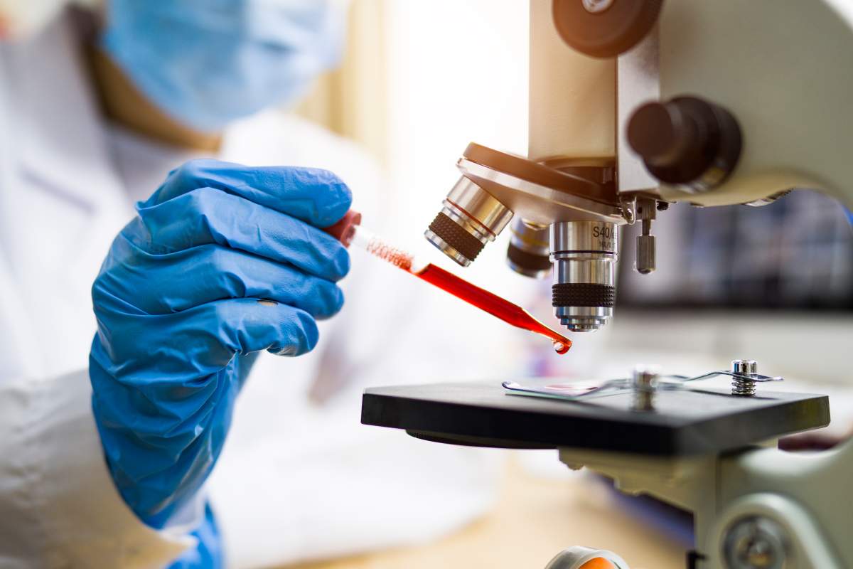 A scientist drops a red substance onto a slide under a microscope.