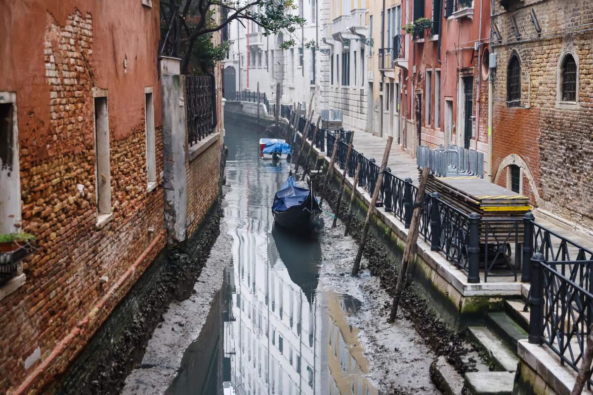 A dry canal in Venice. There is a grounded boat, and the foundation of buildings is visible.
