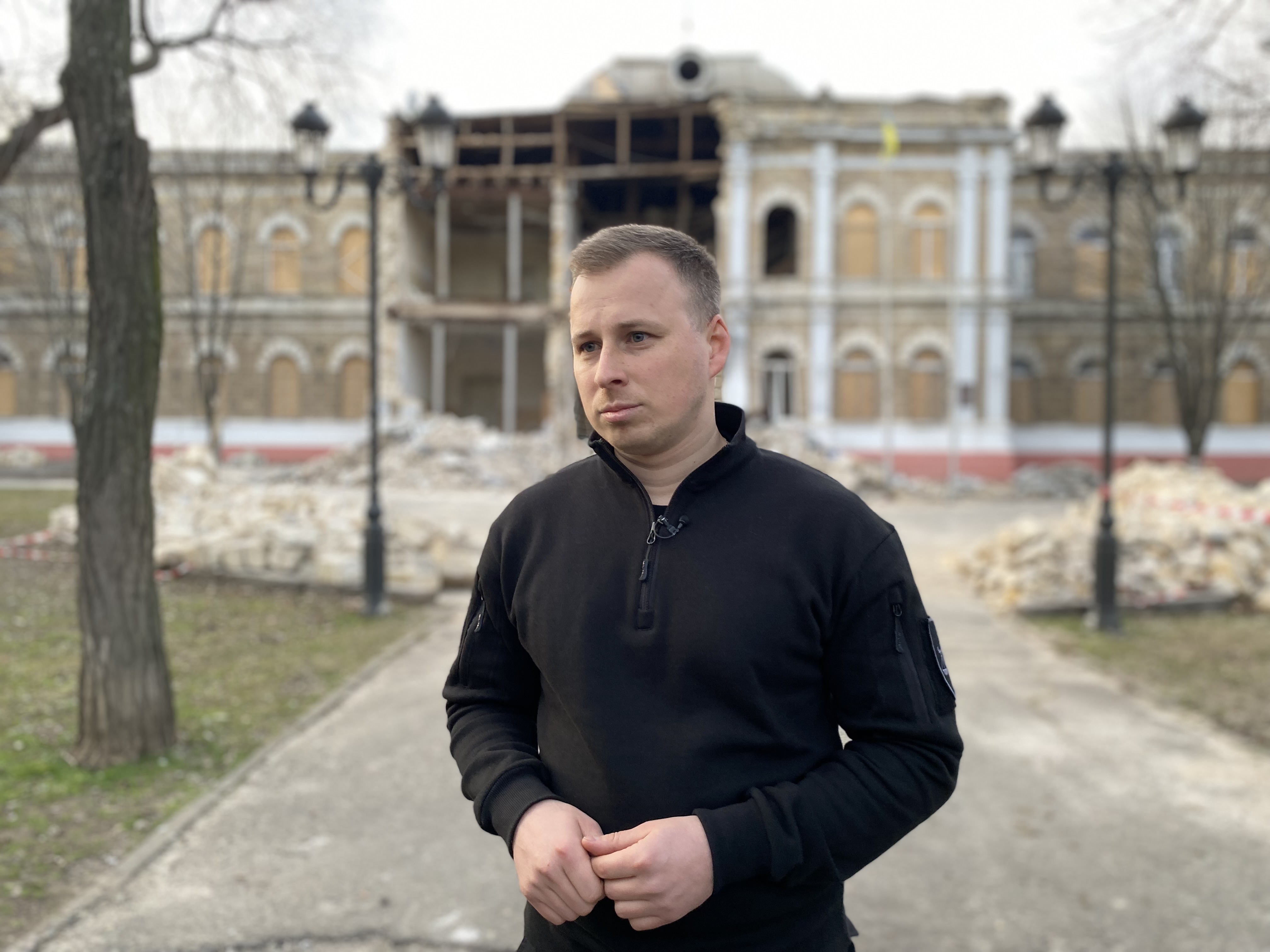 Ukrainian prosecutor Oleksii Lehkyi, in front of a war-damaged building, is investigating a Kherson journalist accused of collaboration.