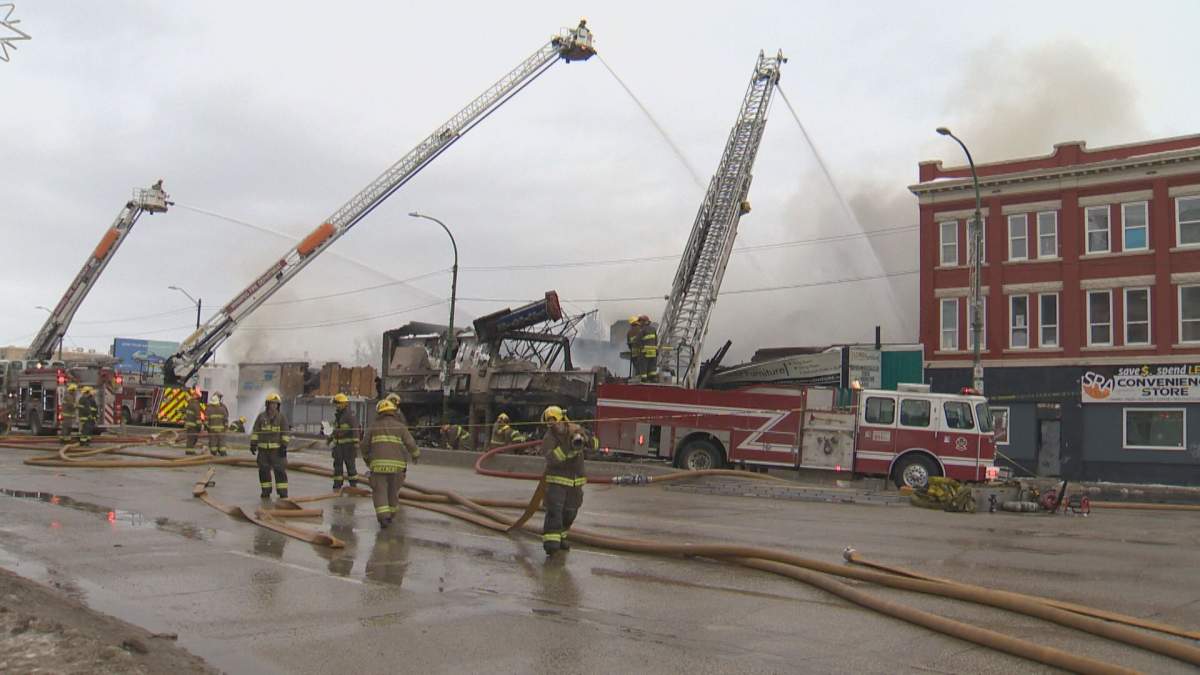 Three aerial ladders shoot water onto a structure fire. Firefighters and hoses are in the foreground, and smoke is in the air.