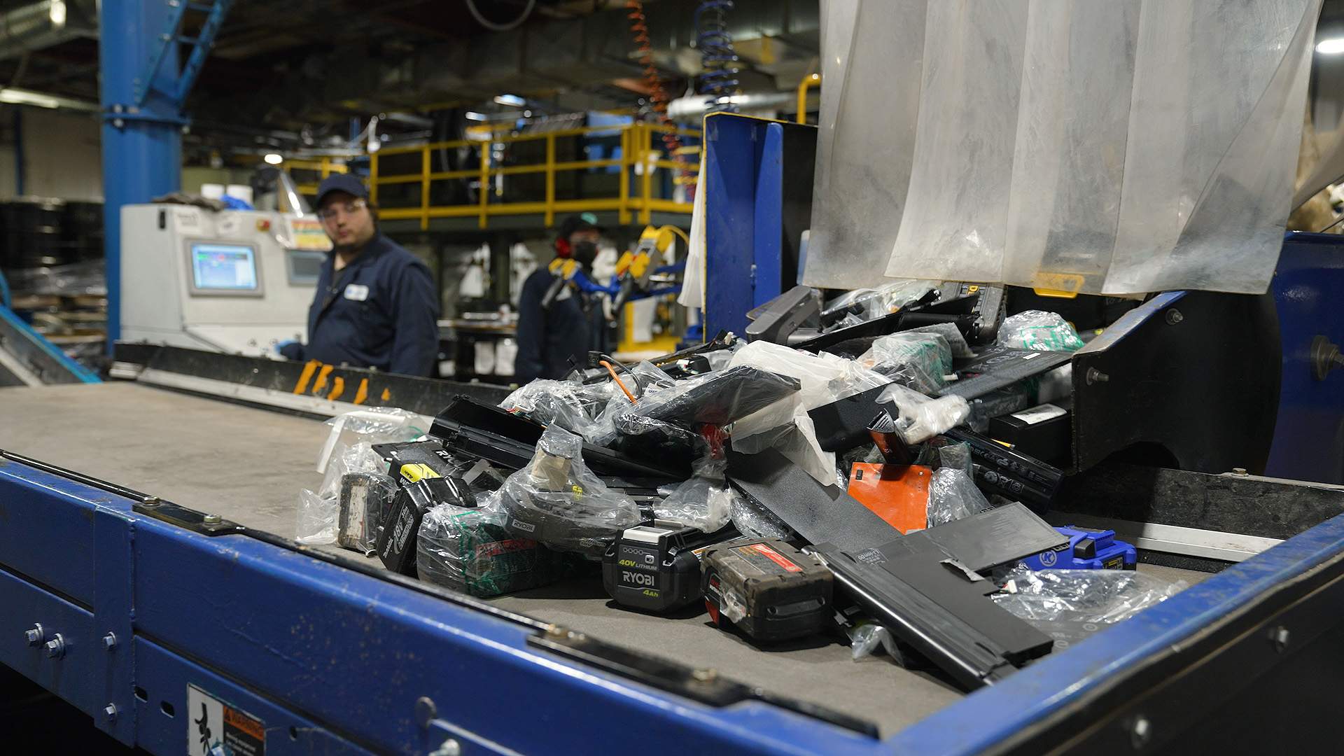 Drill, cellphone, and laptop batteries are dumped onto the conveyor at Li-Cycle's Kingston, ON plant. Each battery must be unwrapped and checked to make sure it is lithium-ion.