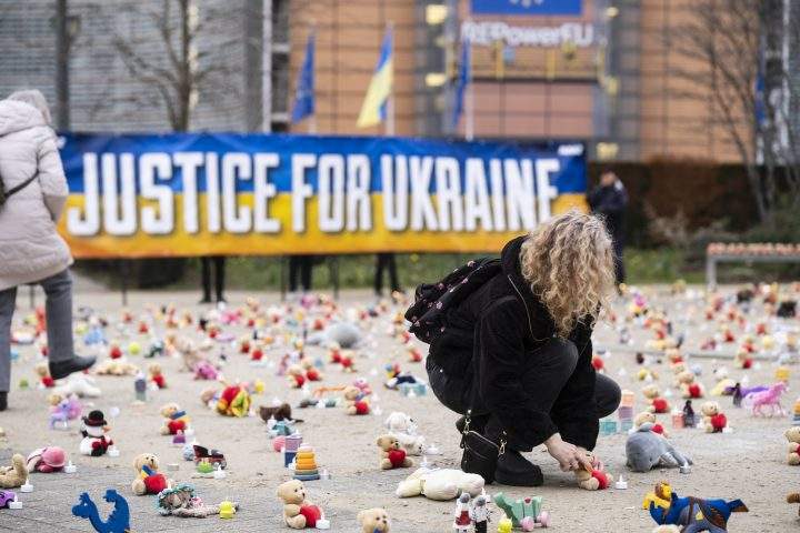 People from U.S.-based non-profit organization Avaaz light candles beside teddy bears in Schuman Roundabout, the heart of the EU district on Feb. 24, 2023 in Brussels, Belgium.