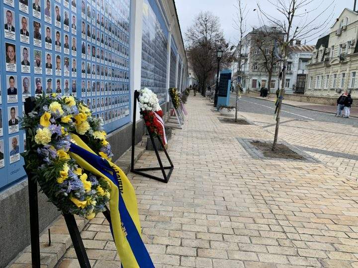Wreaths and flowers adorn a wall covered with photos of soldiers killed during the war in Kyiv on Friday, Feb 24, 2023.