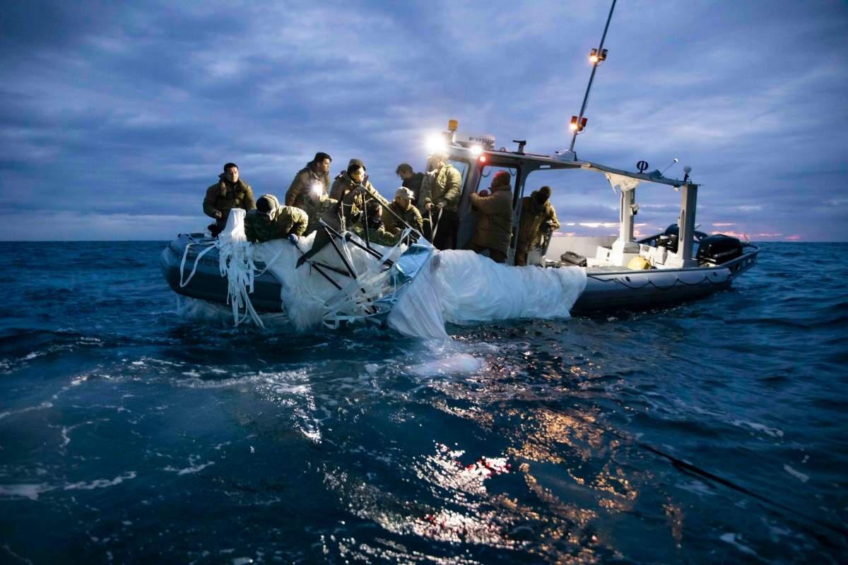 Navy sailors pull debris onto a white boat. It is getting dark and a light in on the ship.