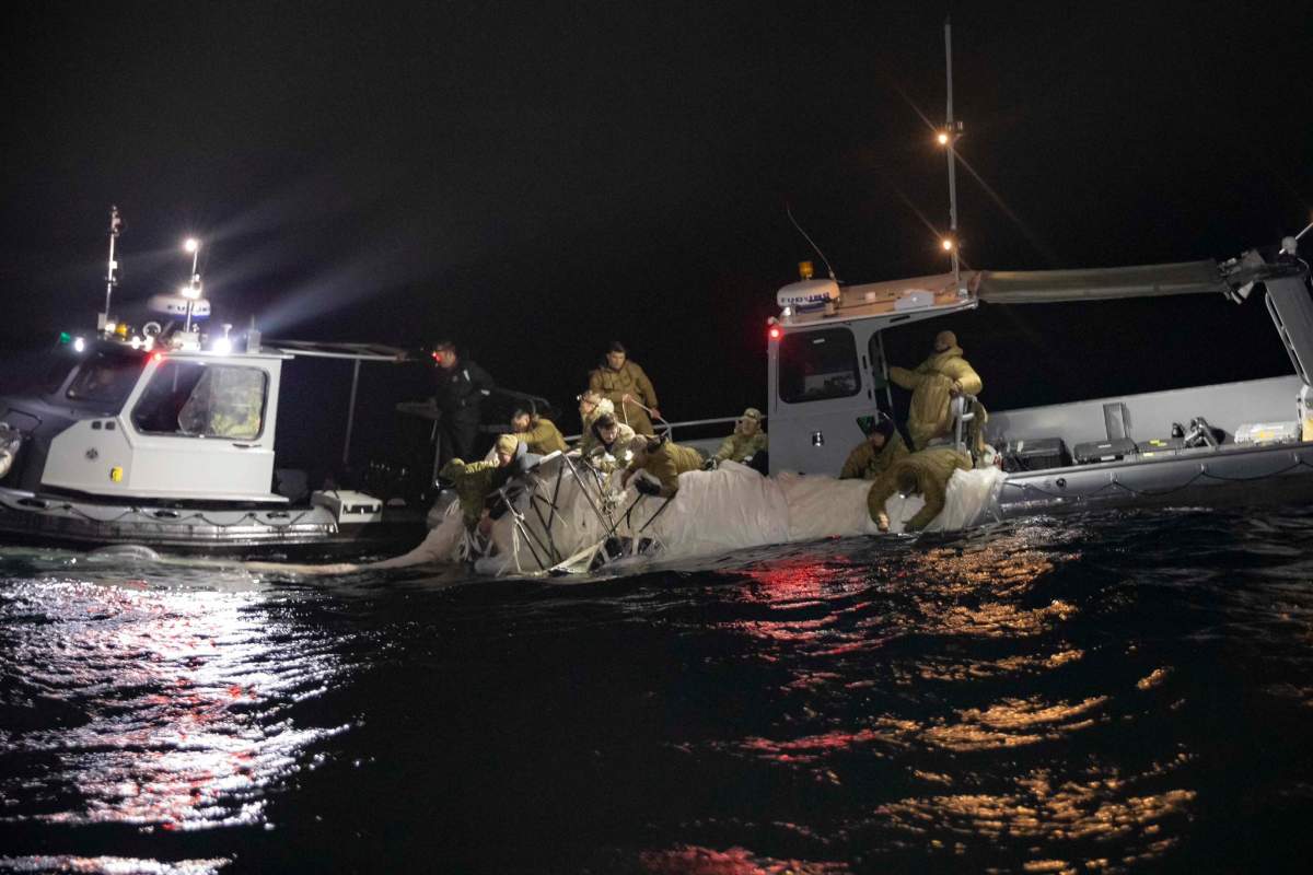 A U.S. Navy boat in the dark. Officials pull material from the water onto the deck.