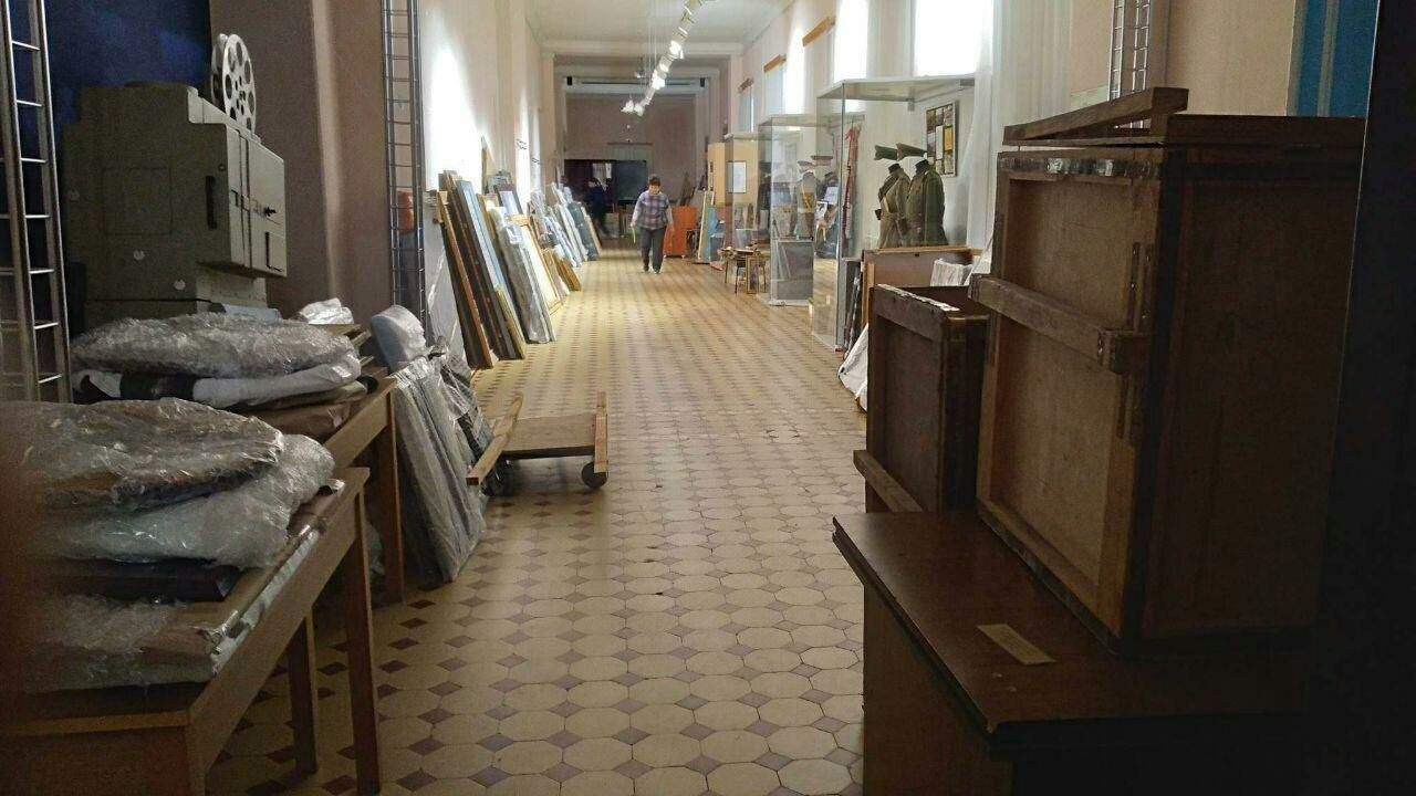 Paintings stolen from Kherson Art Museum lean against walls at museum in Russian-occupied Crimea. To left of woman is “The Ancient Walls of Vilnius,” by Augustunas Savockas.