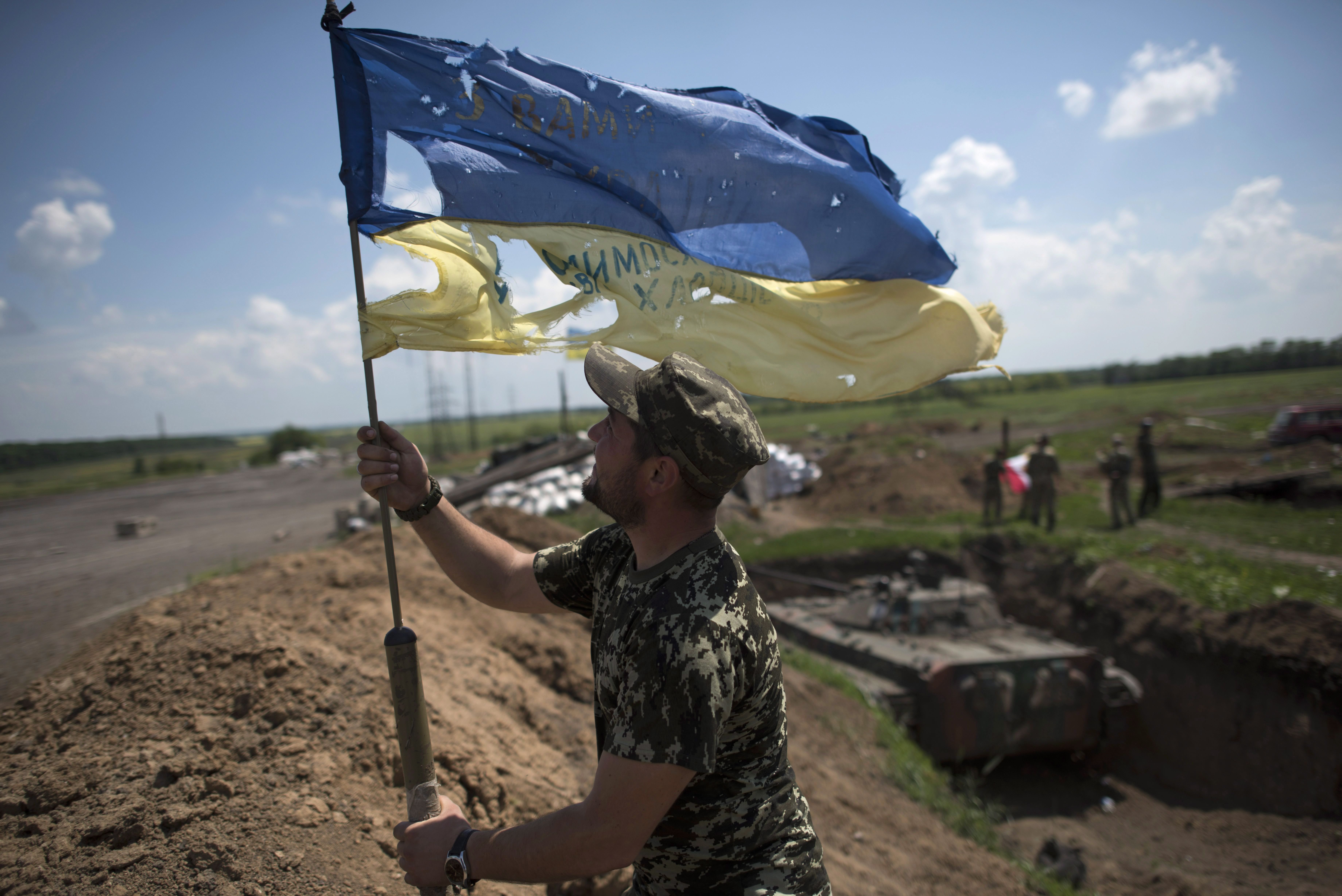A tattered Ukrainian flag is stood up tall in a field.