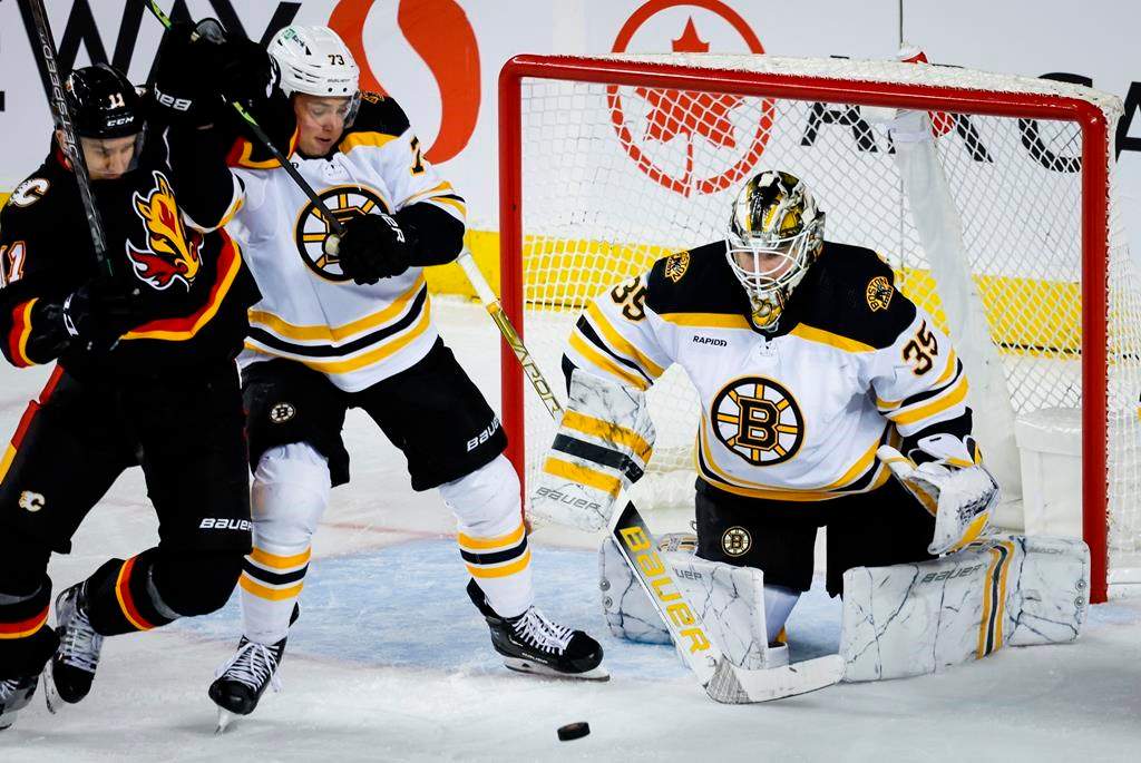 Boston Bruins defenceman Charlie McAvoy, centre, keeps Calgary Flames forward Mikael Backlund, left, away from the puck as goalie Linus Ullmark looks on during second period NHL hockey action in Calgary, Tuesday, Feb. 28, 2023.