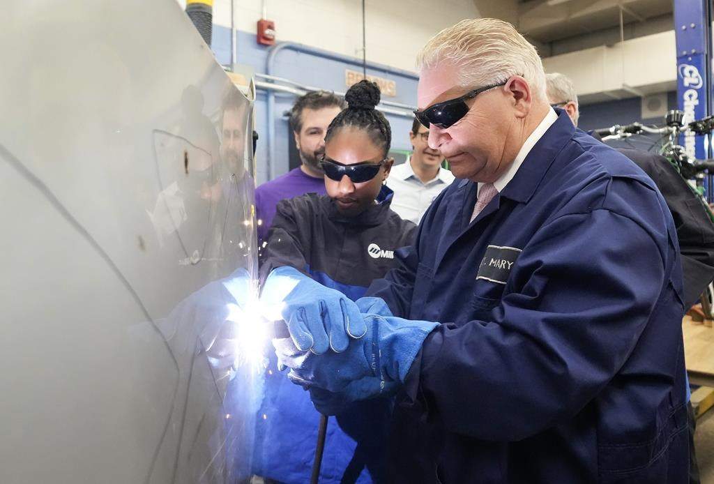 Ontario Premier Doug Ford, right, gets help from grade 11 student Shannon Williams, 16, as they practise plasma welding on a car hood as while visiting St. Mary Catholic Secondary School in Pickering, Ont., on Wednesday, March 8, 2023. Ontario will allow students in Grade 11 to begin working toward their apprenticeships in skilled trades. 