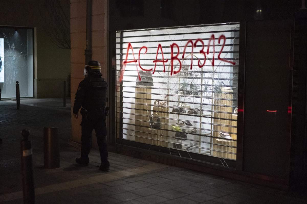 A French riot policeman stands next to a broken shop window during a demonstration in Marseille, southern France, Thursday, March 16, 2023.