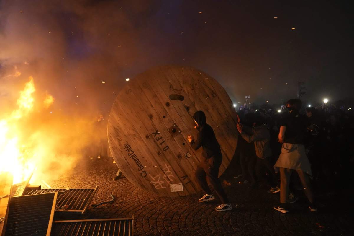 Demonstrators rolls a wooden cable spool to a burning barricade during a protest in Paris, Friday, March 17, 2023. Protests against French President Emmanuel Macron’s decision to force a bill raising the retirement age from 62 to 64 through parliament without a vote disrupted traffic, garbage collection and university campuses in Paris as opponents of the change maintained their resolve to get the government to back down. (AP Photo/Lewis Joly)
