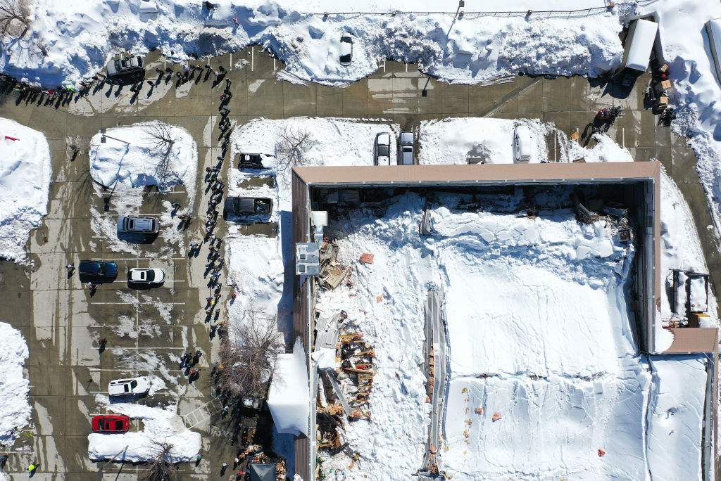 An aerial view of residents (L) waiting in line to receive donated food outside the local grocery store (R), which was severely damaged when its roof collapsed under the weight of several feet of snow, after a series of winter storms in the San Bernardino Mountains in Southern California on March 3, 2023 in Crestline, Calif.