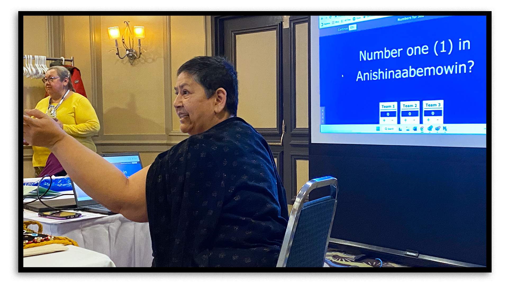 In a hotel’s conference room in Sudbury, two women animate a game of Jeopardy! There’s a projector screen behind them and the question “Number one in Anishinaabemowin?” is on the screen. At the bottom of the screen, the points scored so far by each of the three teams competing in the game are on display.