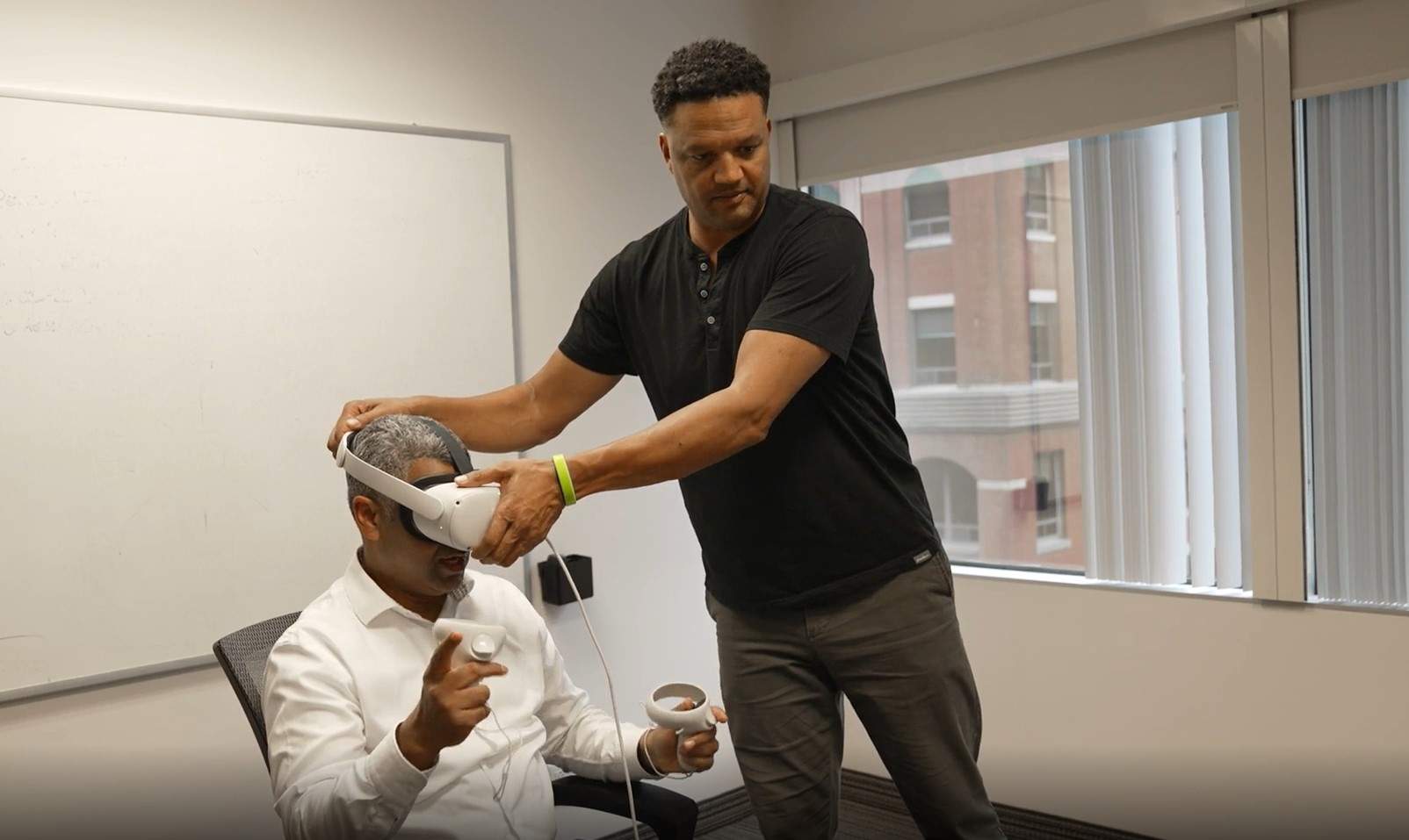 Michael Avis (right) is fitting a VR headset on to a person about to take one of the anti-racism modules he helped to create.