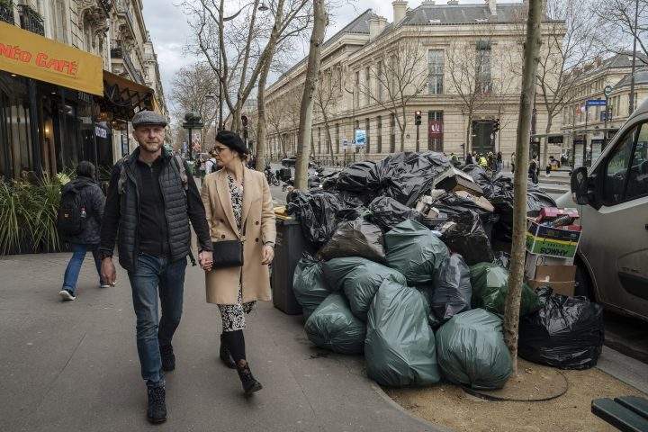 People walk past uncollected garbage in Paris, Monday, March 13, 2023. (AP Photo/Lewis Joly)