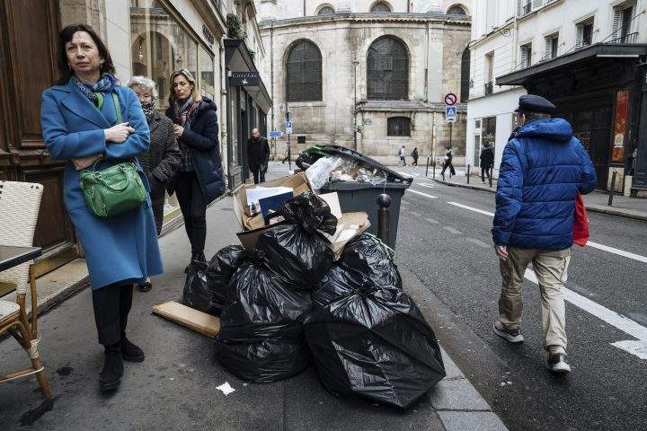 People walk past uncollected garbage in Paris, Monday, March 13, 2023. (AP Photo/Lewis Joly)