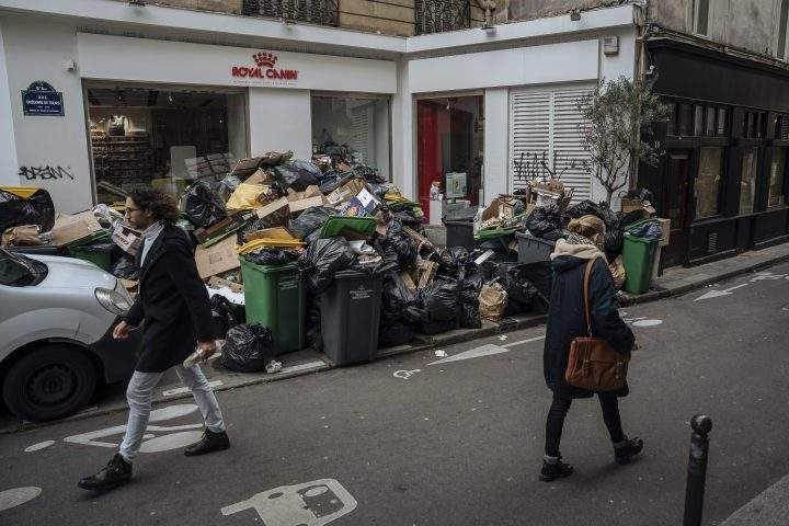 People walk past uncollected garbage in Paris, Monday, March 13, 2023. (AP Photo/Lewis Joly)