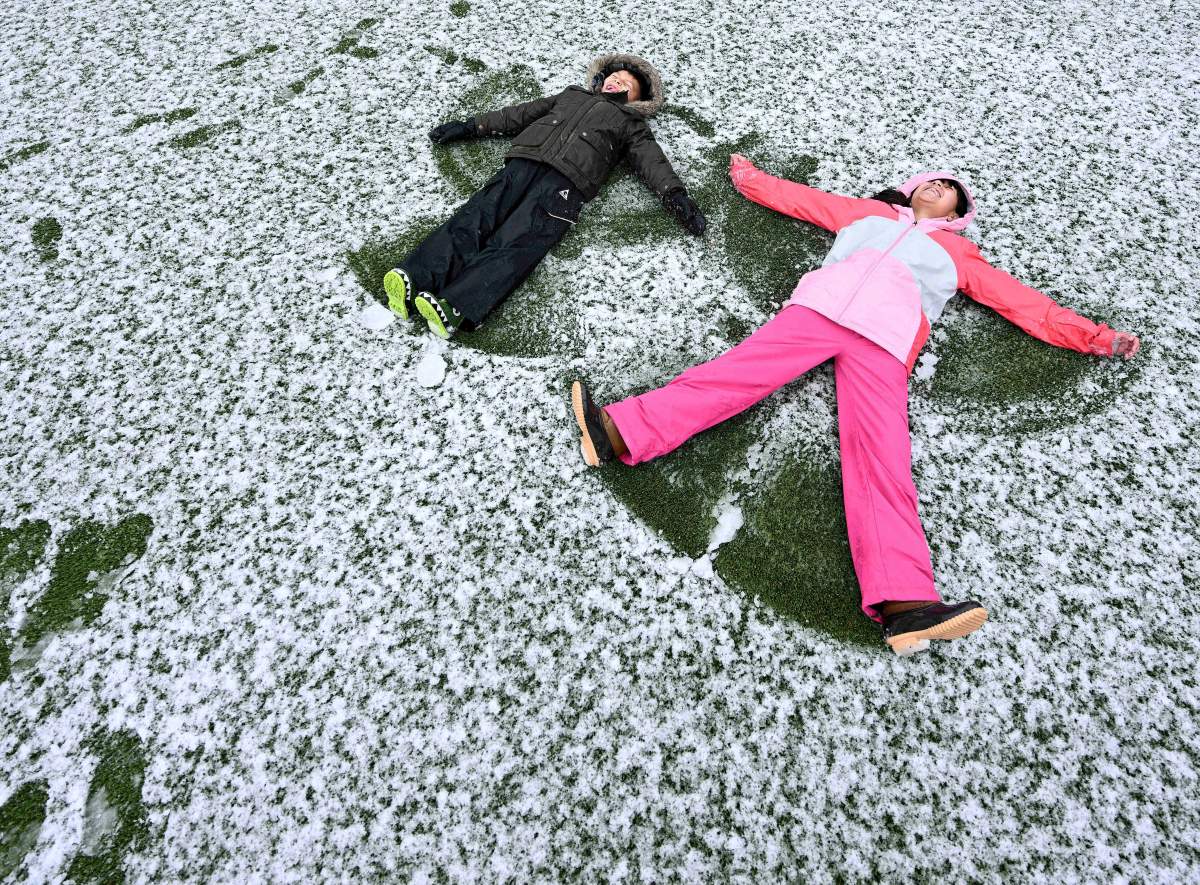 Two children make snow angels in a faint dusting of snow over still-green grass underneath in southern California.
