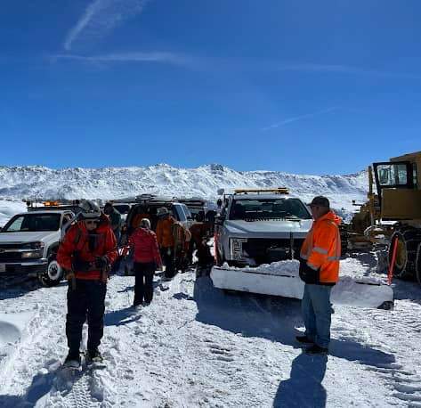 Search and rescue crew alongside vehicles on a snowy road.